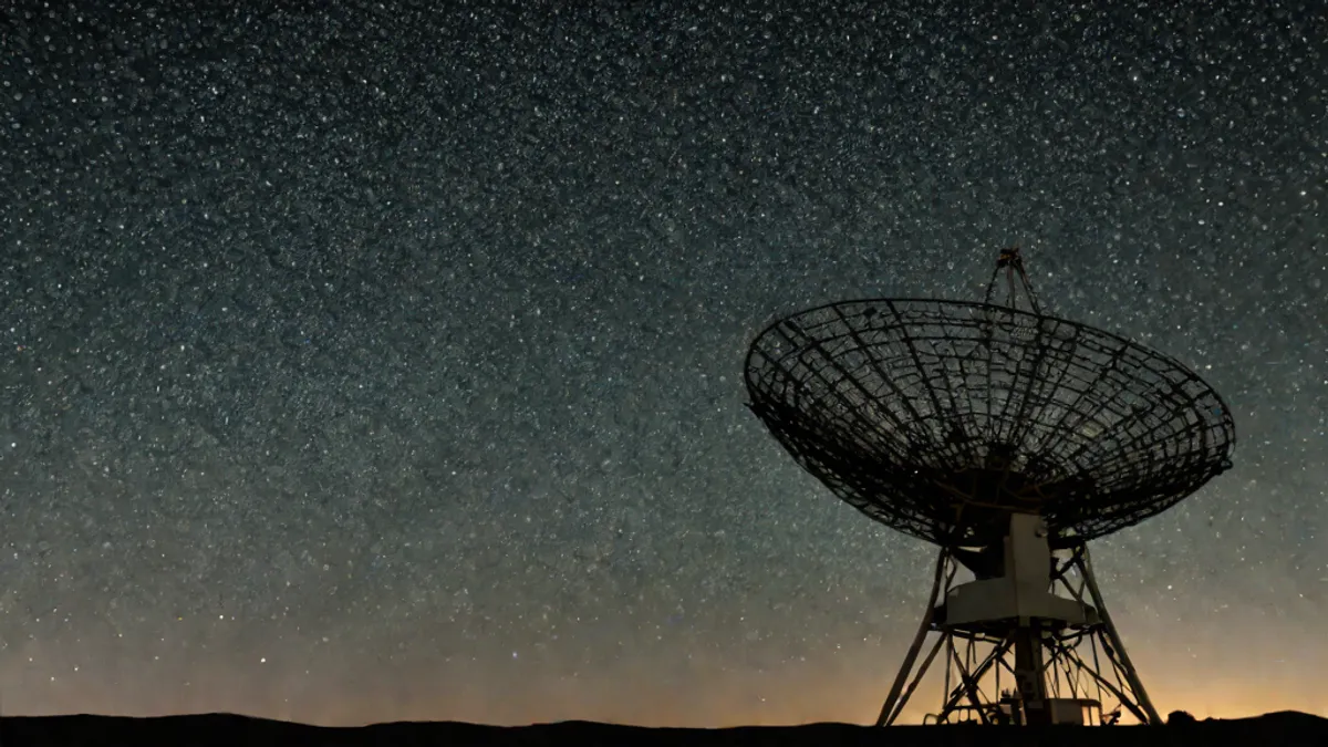 Gran radiotelescopio apuntando hacia la Vía Láctea en un cielo nocturno estrellado.