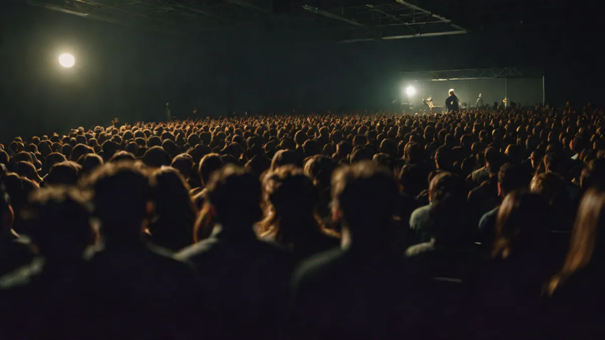 Multitud de personas sentadas de espaldas en un auditorio en penumbra.
